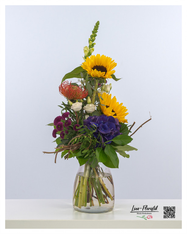 Ein Blumenstrauß im Sommer, der leuchtende Sonnenblumen, violette Hortensien und Santini mit exotischer Protea vereint und so eine frische, lebendige Atmosphäre verbreitet.