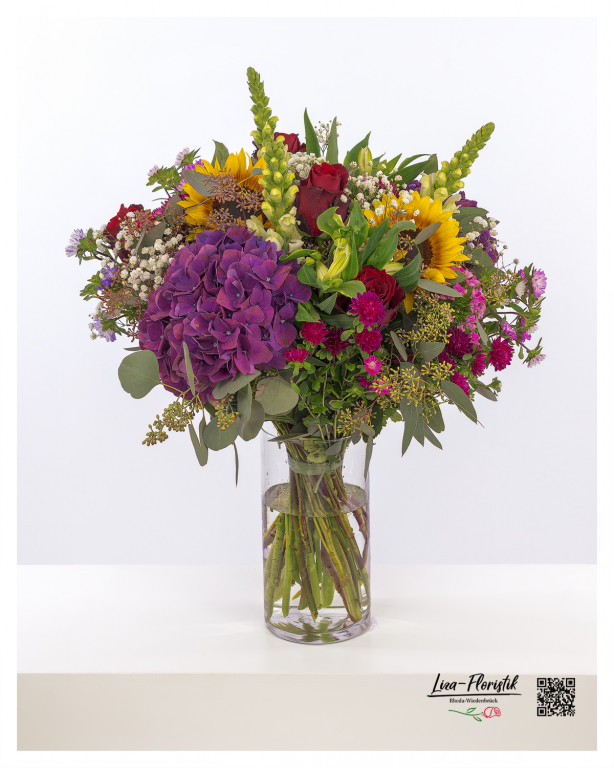 Bunter Blumenstrauß – Üppig bestückt mit Hortensien, Sonnenblumen und Rosen mit violetter Hortensie, strahlenden Sonnenblumen, roten Rosen, Nelken, Astern, Löwenmäulchen, Thlaspi, Eukalyptus und zartem Schleierkraut – eine vielfältige Komposition für farbenfrohe und besondere Momente.