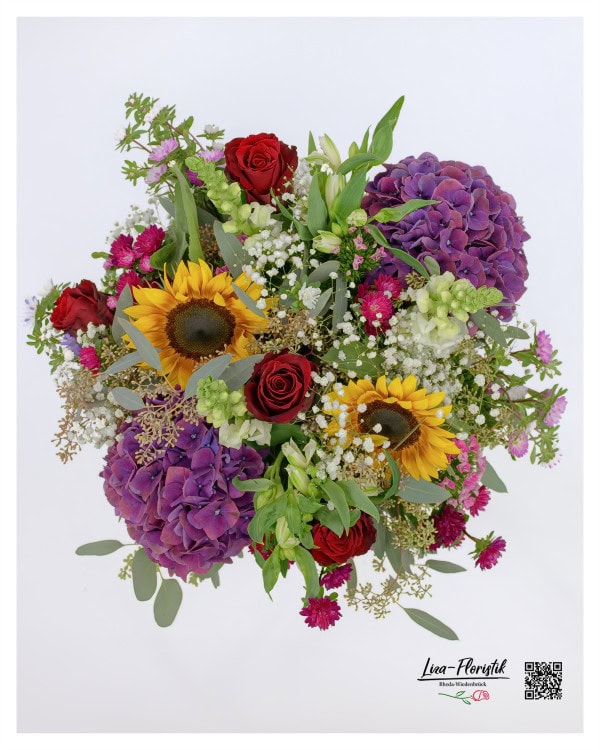 Eine beeindruckende Draufsicht auf den voluminösen Strauß, der mit leuchtenden Sonnenblumen, violetten Hortensien, roten Rosen, Nelken, Löwenmäulchen, Eukalyptus, Astern und zartem Schleierkraut prachtvoll arrangiert ist.