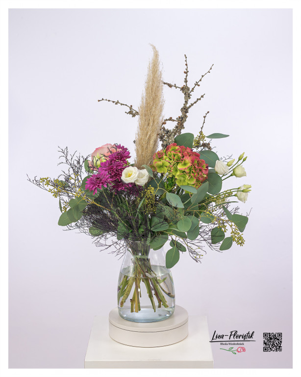 Dieser einzigartige Blumenstrauß mit Pampasgras kombiniert natürliche Eleganz mit lebendiger Farbpracht. Das zarte Pampasgras bildet den Mittelpunkt und verleiht dem Arrangement eine luftige, leichte Ausstrahlung. Grüne und rosa Hortensien, elegante Rosen und lebhafte Chrysanthemen schaffen ein harmonisches Farbspiel. Zarter Lisianthus, Eukalyptusblätter und dekorative Lärchenzweige runden den Strauß ab und verleihen ihm eine besondere Struktur und Tiefe. Ein stilvoller Blickfang für jedes Ambiente!