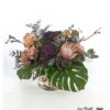 Ein prachtvoller Blumenstrauß mit exotischer Königsprotea, dekorativen Lärchenzweigen, edlen Hortensien, zarten Chrysanthemen, frischem Eukalyptus, filigraner Statice und imposanten Monsterablättern – eine harmonische Kombination aus natürlichen Farben und Strukturen, die Eleganz und Exotik vereint.
