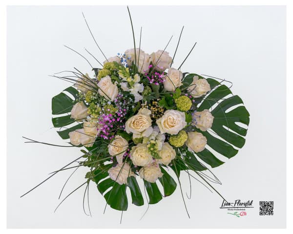 Großer Blumenstrauß in Draufsicht, kunstvoll gebunden mit 20 cremeweißen Ecuador Rosen der Sorte Mondial, saisonalem Schneeball, weißen Löwenmäulchen und farbigem Schleierkraut in Rosa, Violett und Blau. Umrahmt von dekorativem Blattgrün, darunter große Monstera-Blätter und filigrane Gräser für eine tropisch-elegante Optik.