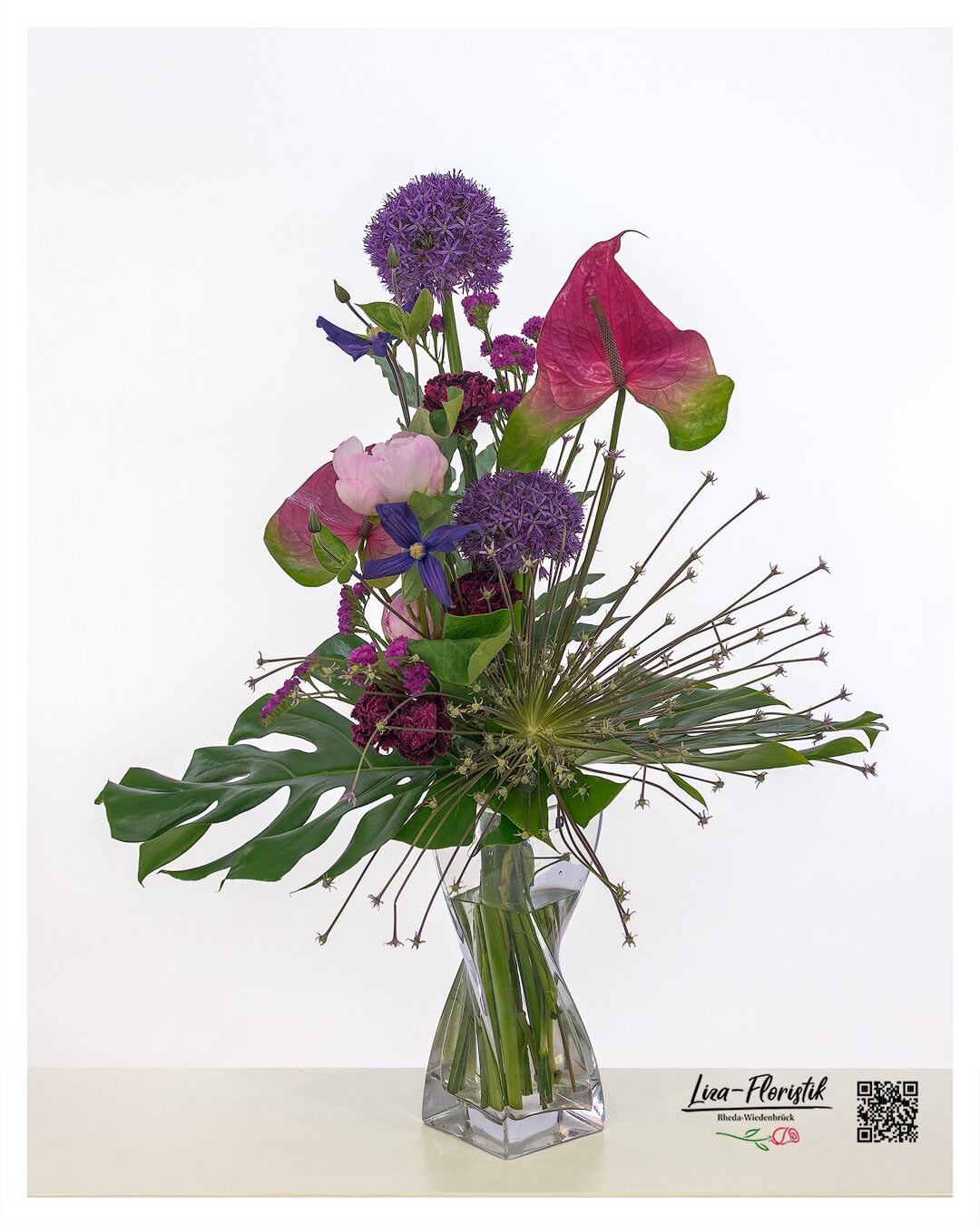 Moderner Blumenstrauß mit auffälligem Allium, darunter auch eine sternförmig explodierende Allium-Schuberti-Blüte. Ergänzt wird das Arrangement durch leuchtend pinke Anthurien, zarte rosa Pfingstrosen, tiefviolette Clematis und kleine, filigrane Statice-Blüten – kombiniert mit großflächigem Grün für einen expressiven, skulpturalen Look.
