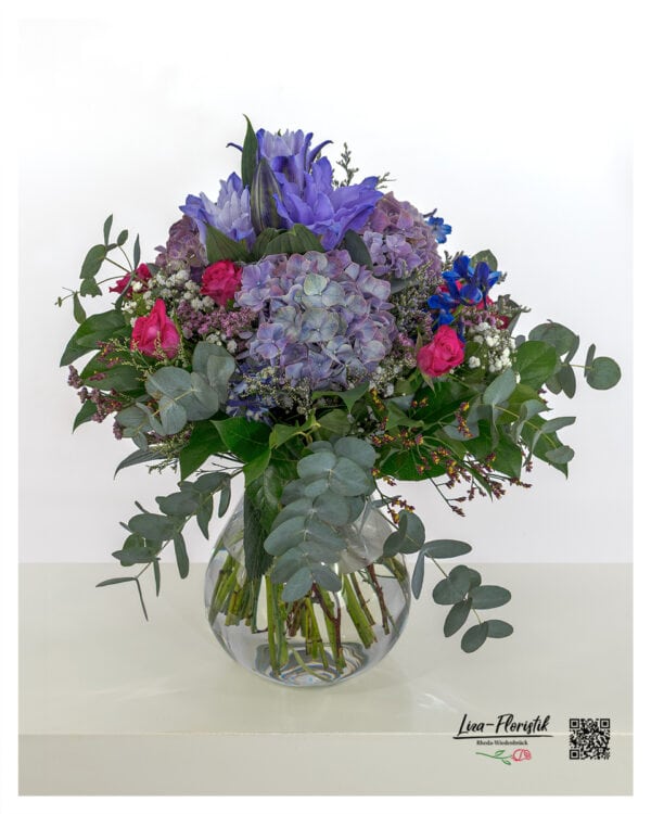 Üppiger Blumenstrauß mit lila Hortensien, pinken Rosen, violetten Lilien, blauem Rittersporn, Schleierkraut, Statice und frischem Eukalyptus – ideal als Geschenk oder Dekoration.