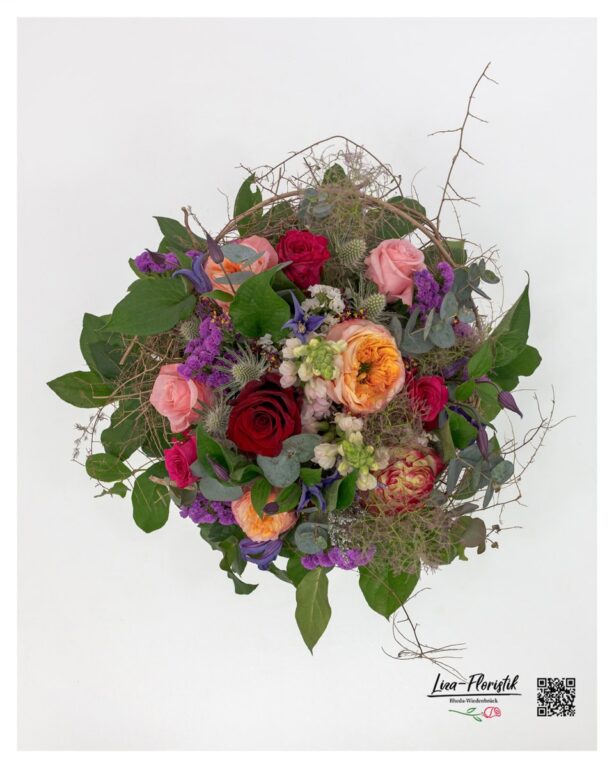 Draufsicht auf das Arrangement – verschiedene Rosenfarben, Clematis und Disteln in einem kreativem, kunstvollen Gesamtbild.