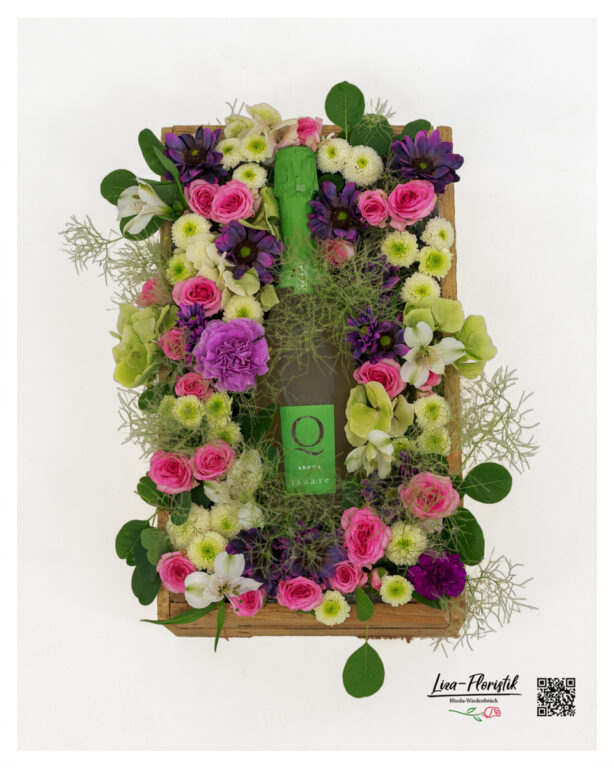 Blumengesteck in rustikaler Holzkiste mit Sekt, rosa Rosen, violetten Blüten, cremeweißen Santini und zartem Perückenstrauch