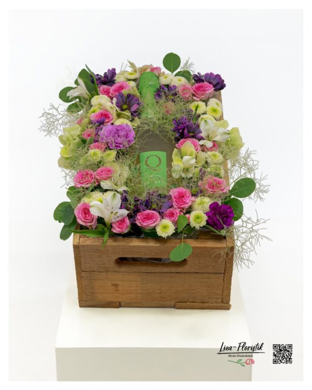 Janare Q Spumante als Mittelpunkt eines exklusiven Blumengeschenks in rustikaler Holzkiste